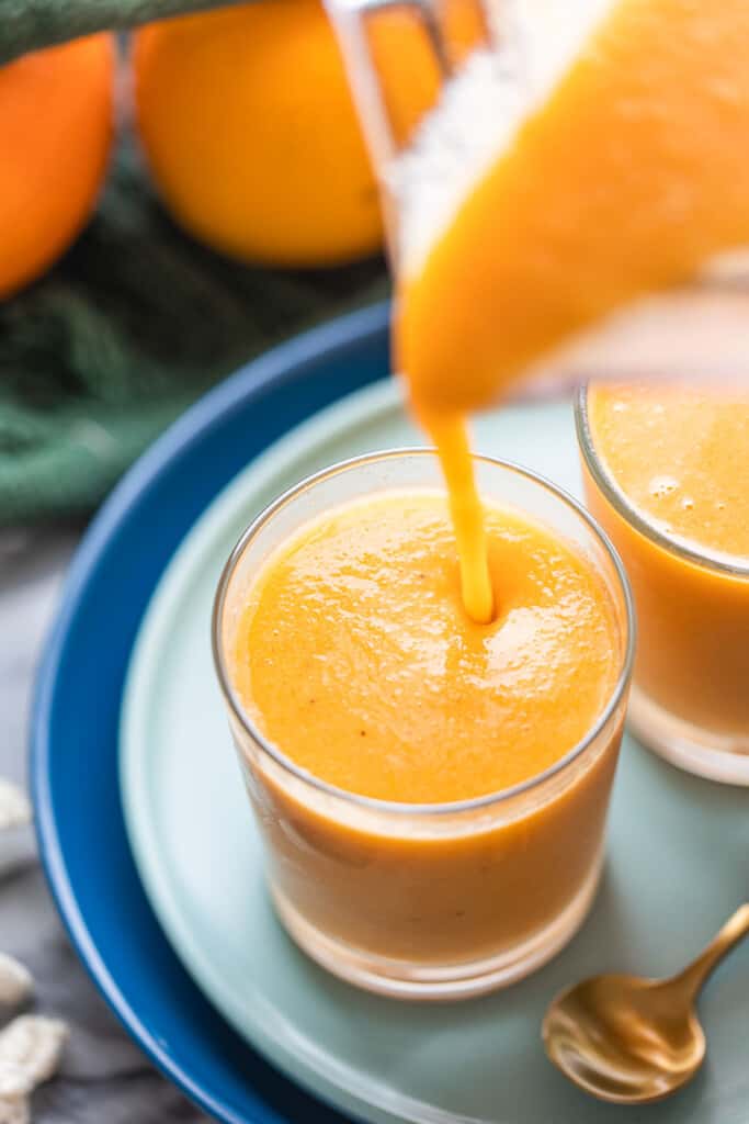 orange creamsicle smoothie pouring into a small glass from blender