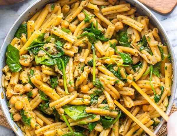serving tongs mixing together za'atar spiced pasta with chickpeas in serving pan
