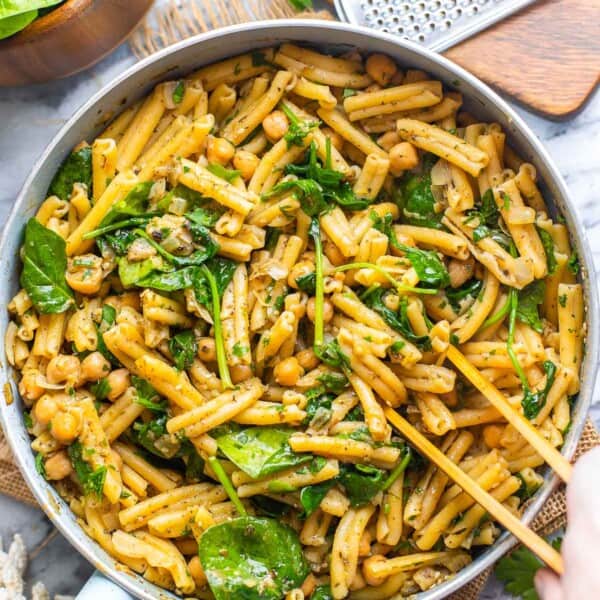 serving tongs mixing together za'atar spiced pasta with chickpeas in serving pan
