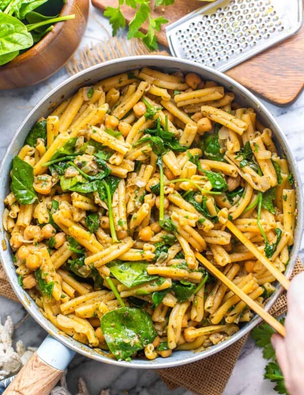 serving tongs mixing together za'atar spiced pasta with chickpeas in serving pan