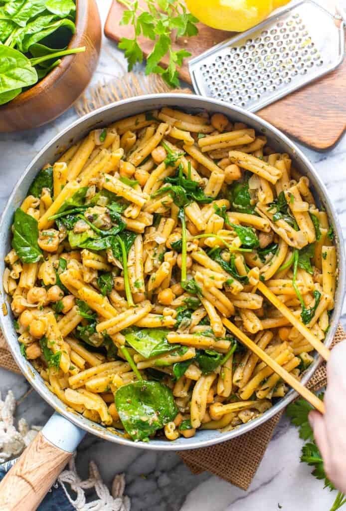 serving tongs mixing together za'atar spiced pasta with chickpeas in serving pan