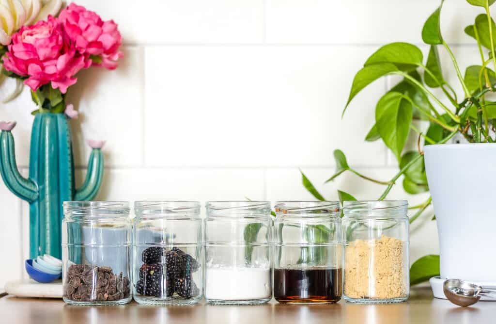 1/2 cup of five different ingredients in identical cups to show the difference in amounts: chocolate chips, blackberries, flour, maple syrup and brown sugar