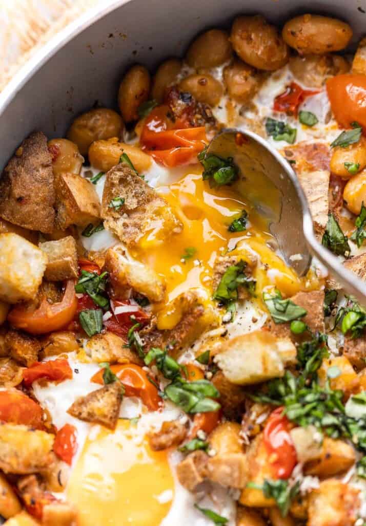 a spoon breaking into a runny egg yolk in a Burst Cherry Tomatoes & White Bean Egg Skillet