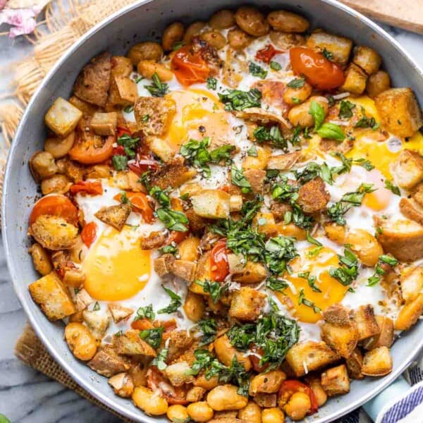 Bust Cherry Tomatoes & White Bean Egg Skillet topped with basil and surrounded by cherry tomatoes and basil