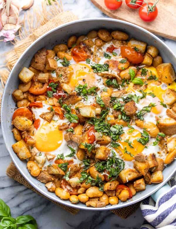 Bust Cherry Tomatoes & White Bean Egg Skillet topped with basil and surrounded by cherry tomatoes and basil