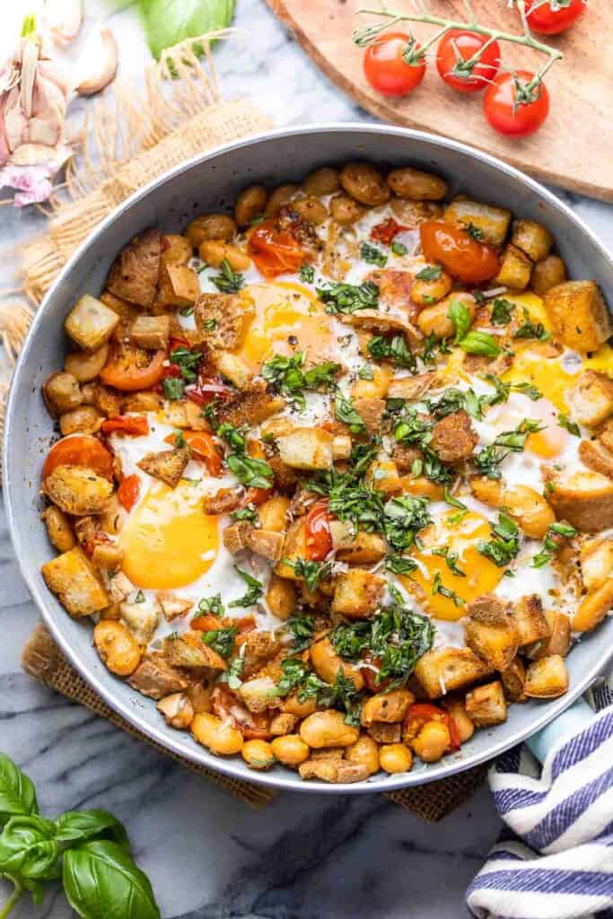 Burst Cherry Tomatoes & White Bean Egg Skillet topped with basil and surrounded by cherry tomatoes and basil