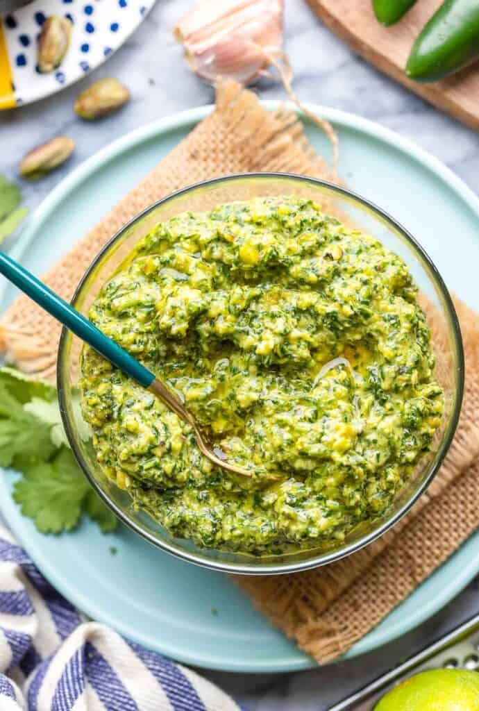 cilantro lime pesto with a spoon in a bowl on a plate with fresh cilantro leaves