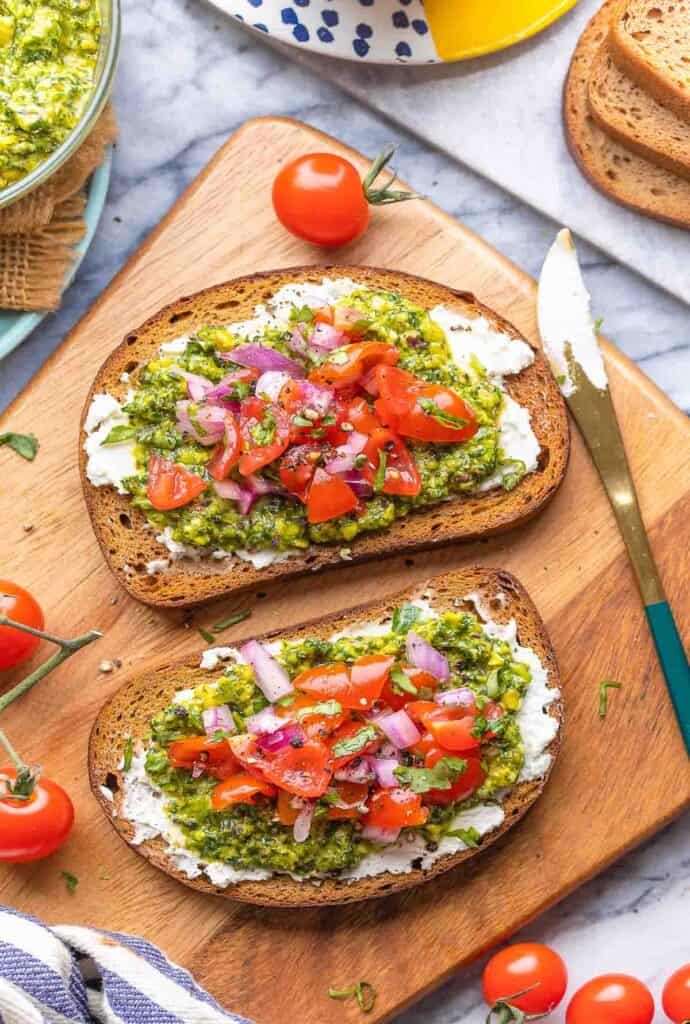 pesto toast and tomato salsa next to a tub of cream cheese and loose tomatoes