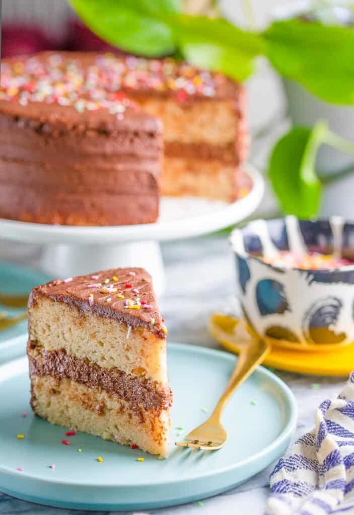 a slice of vegan vanilla cake with chocolate frosting on a plate