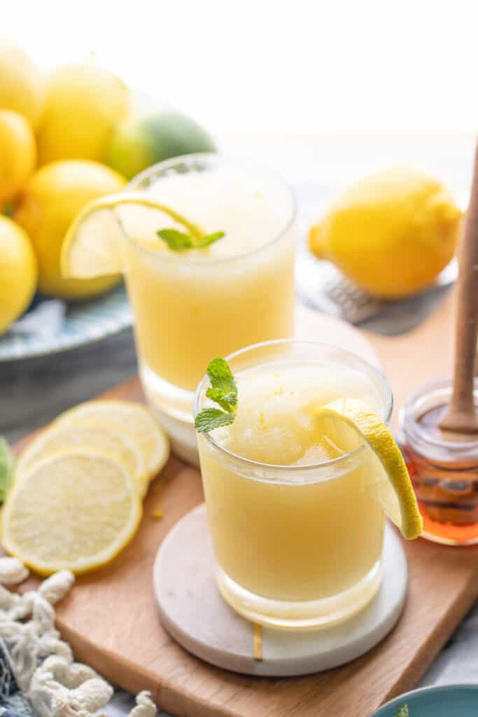 a couple of glasses of frozen lemonade on a serving board with lemon slices