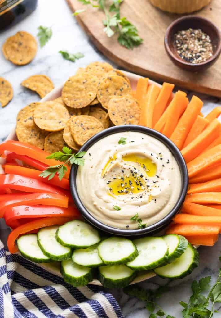 hummus on a platter with crackers and sliced veggies