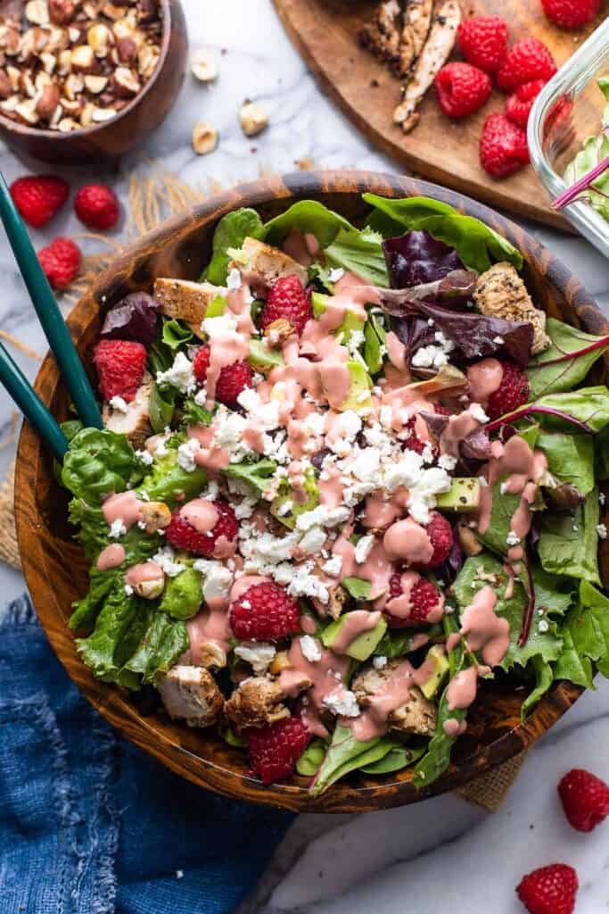 chicken-raspberry-salad with chopped chicken, hazelnuts, and avocado in a wooden salad bowl with a raspberry dressing and crumbled feta on top