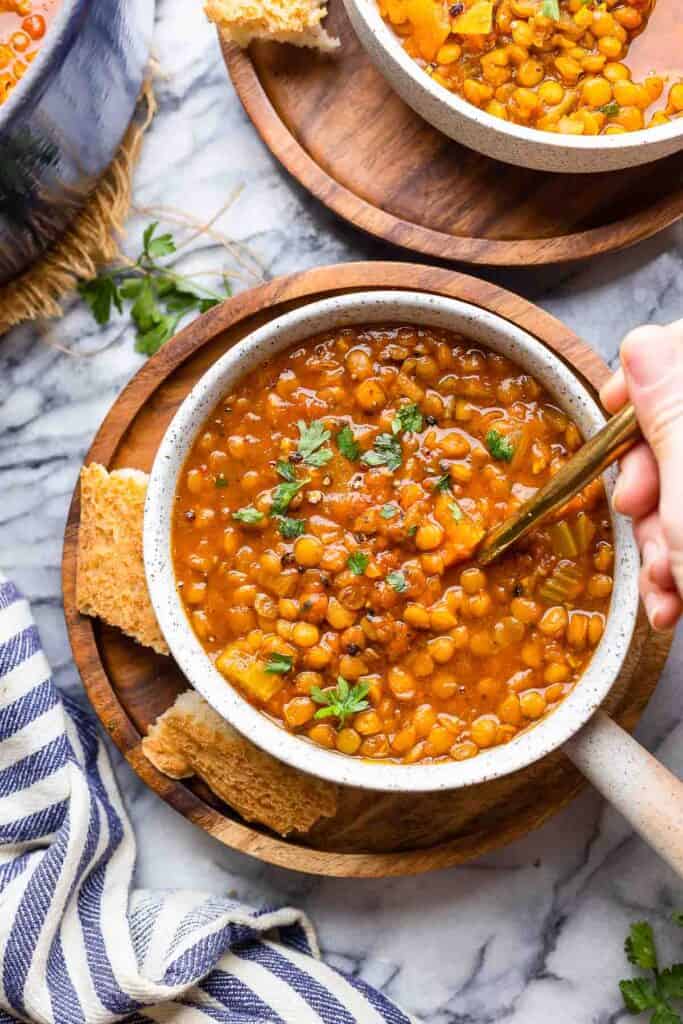 a spoon scooping up some Curried Tomato Lentil Soup on a wooden plate with a side of bread