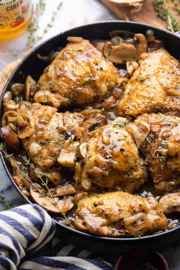 Apple Cider Braised Chicken Thighs in a cast iron pan topped with fresh thyme