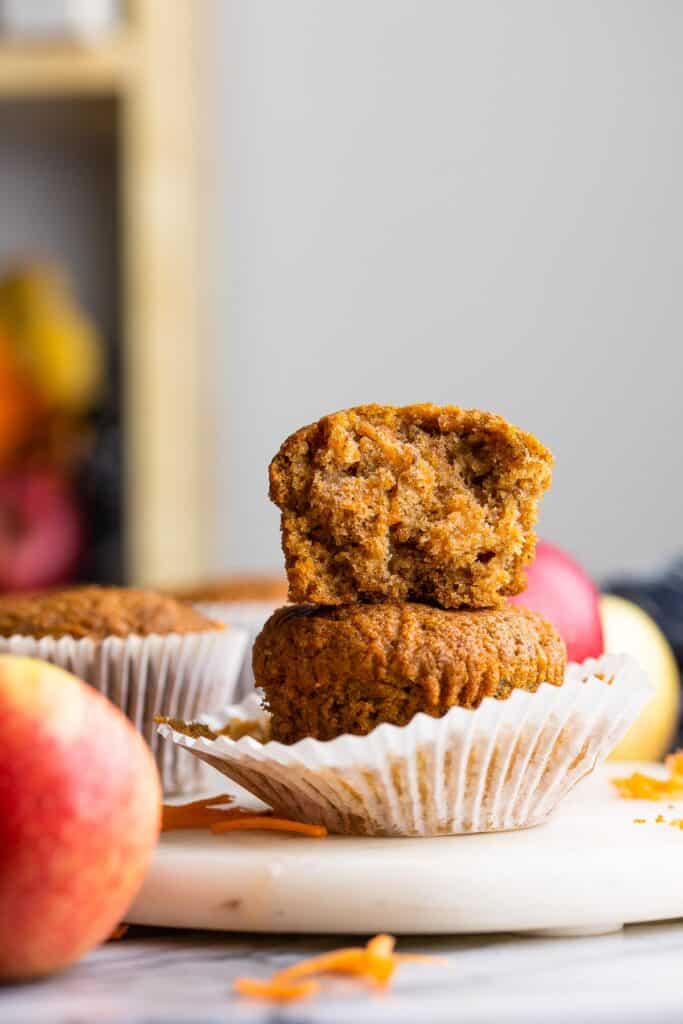 one Carrot & Apple Flaxseed Muffin on top of another - the top muffin with a bite taken out of it