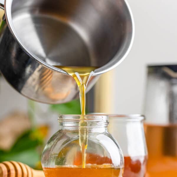 a milk pot pouring a honey simple syrup into a small jar