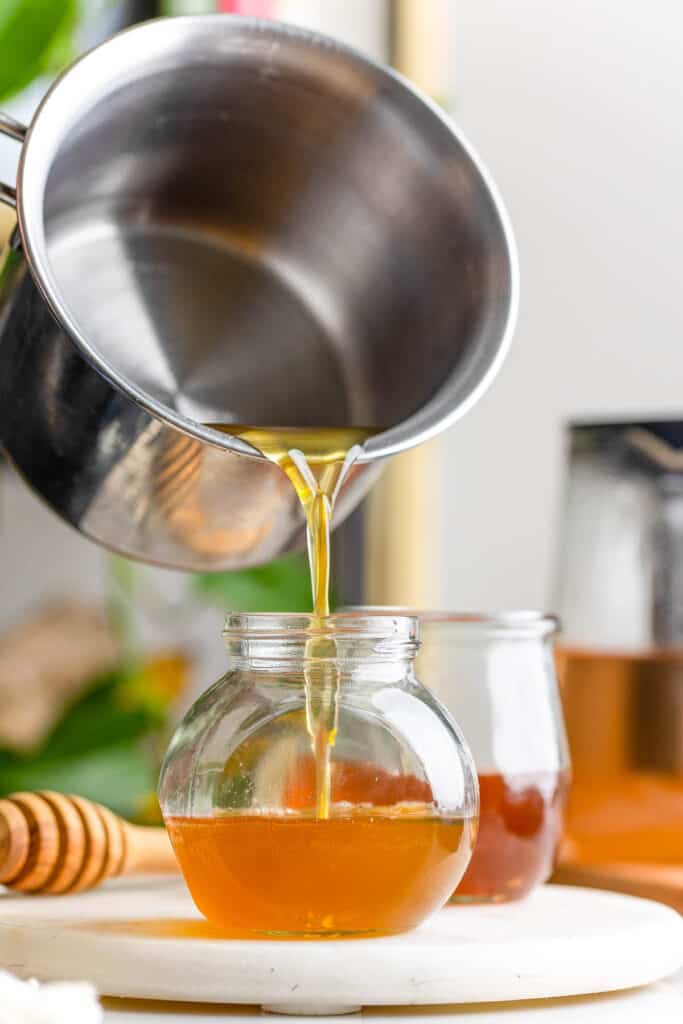 a milk pot pouring a honey simple syrup into a small jar