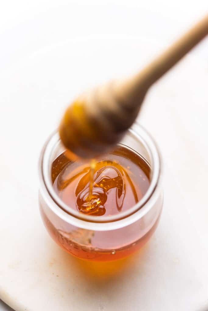 honey running off of a honey dipper in a jar full of honey