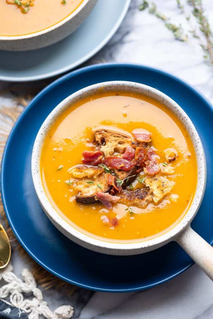 instant pot butternut soup topped with bacon bits, croutons and fresh thyme in a soup bowl on a plate