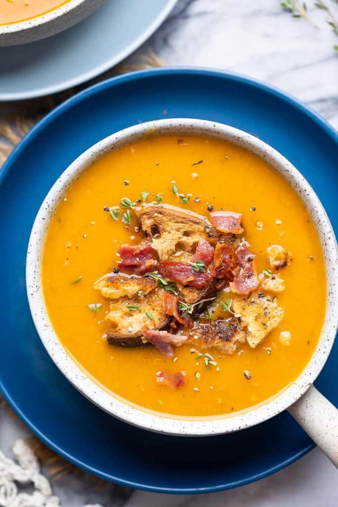 instant pot butternut soup topped with bacon bits, croutons and fresh thyme in a soup bowl on a plate