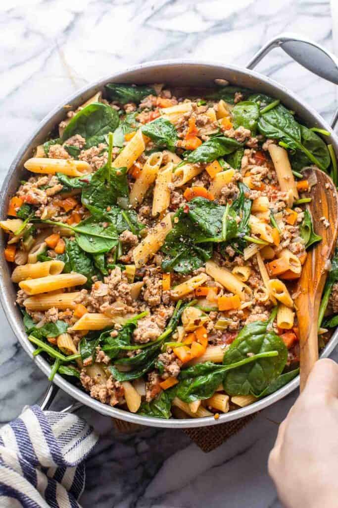 a spoon mixing up a skillet full of ground turkey pasta with wilted spinach 