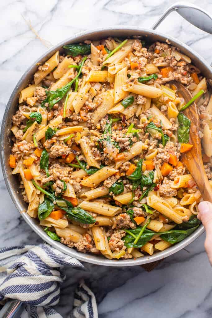 ground turkey pasta in a large skillet with a serving spoon scooping out a serving