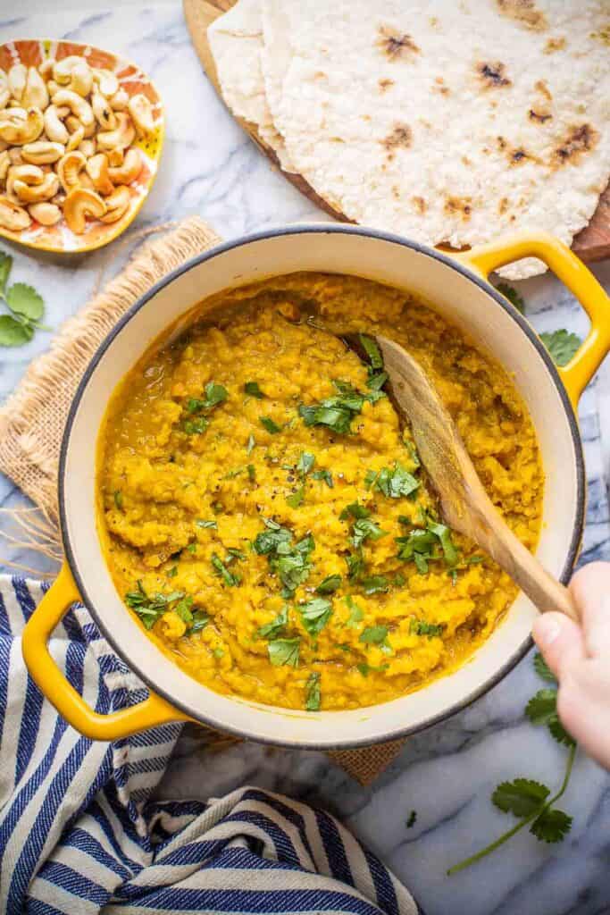 a serving spoon scooping up Red Lentil Dahl in a pot topped with fresh cilantro