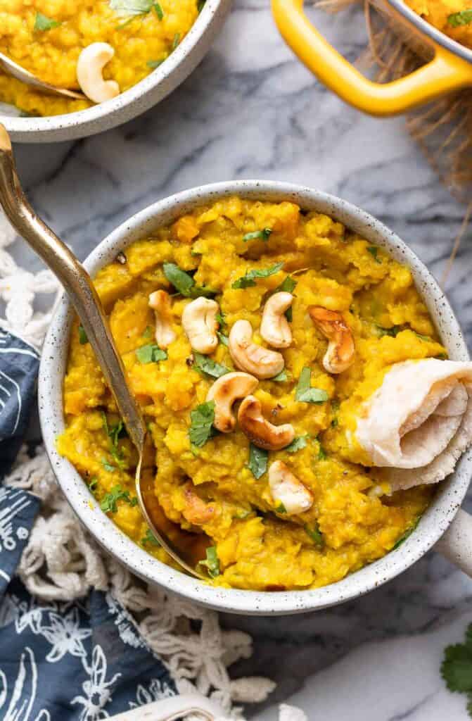 Red Lentil Dahl in a bowl topped with toasted cashews and chapti