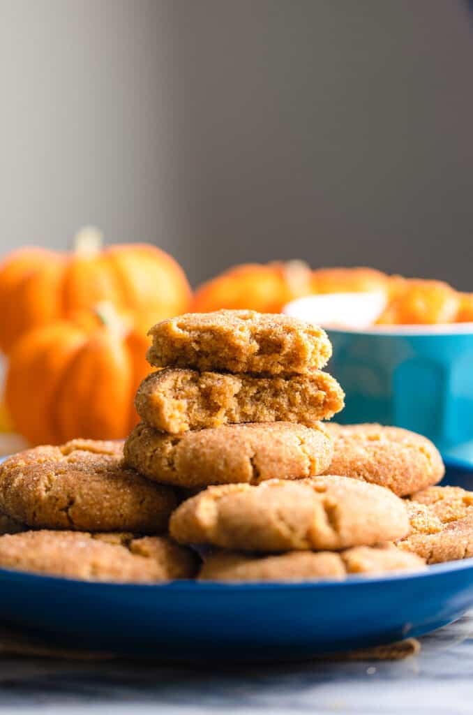pumpkin snickerdoodles piled on a plate with the top cookie broken in half 
