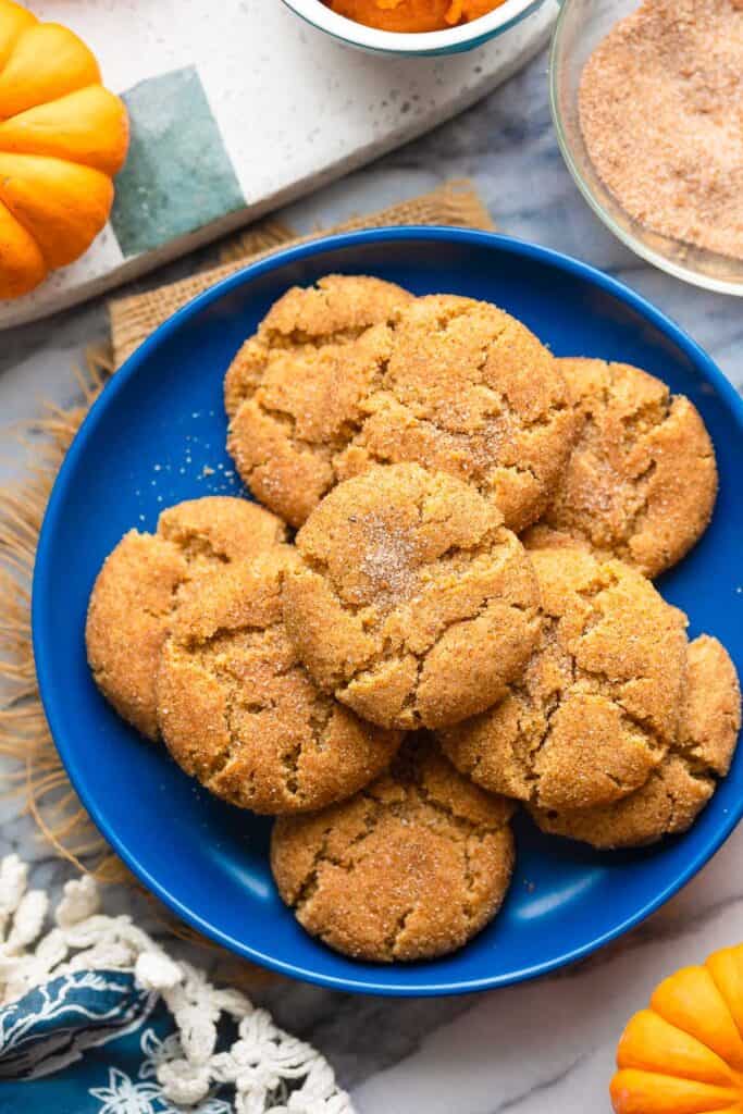 a plate of pumpkin snickerdoodles surrounded by baby pumpkins and a bowl of cinnamon sugar