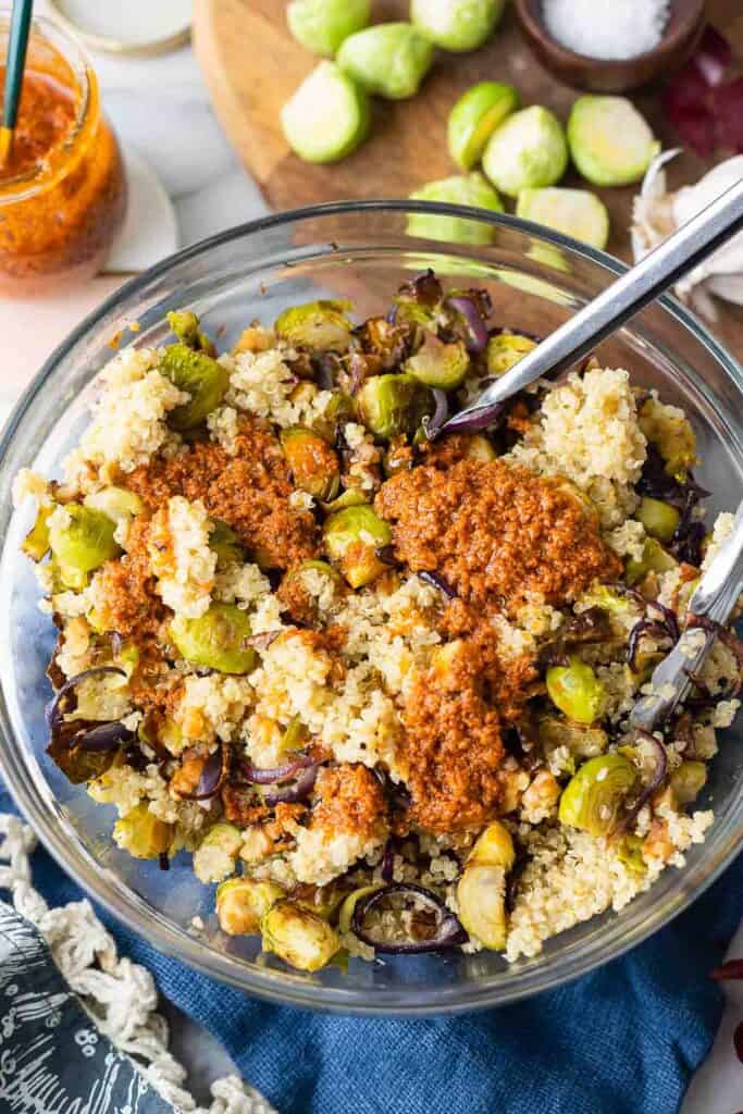 a salad bowl with roasted brussels sprouts, red onions and quinoa topped with a red pesto vinaigrette 
