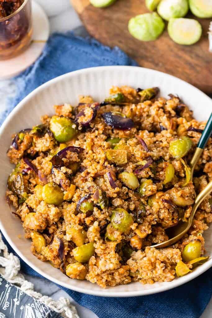 Roasted Brussels Sprouts Quinoa Salad in a serving bowl with serving spoons and halved brussels sprouts in the back