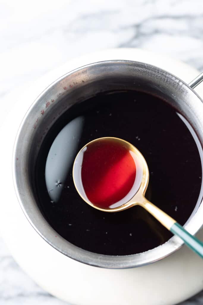 a spoon in a milk pan full of freshly simmered Homemade Grenadine Syrup 