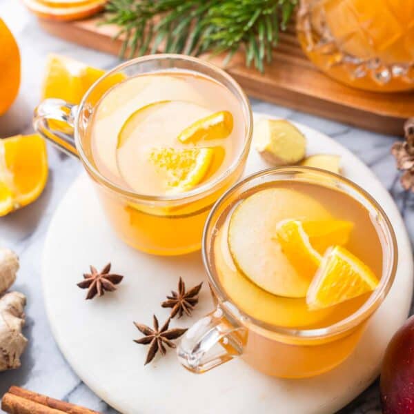 two mugs of apple pear cider on a plate with sliced fruit inside