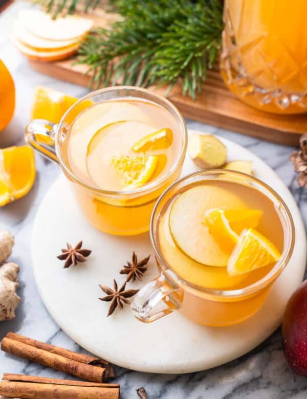 two mugs of apple pear cider on a plate with sliced fruit inside