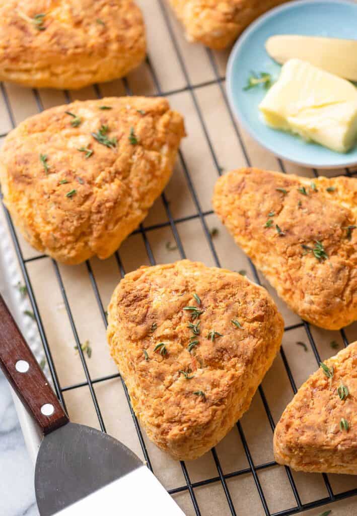 freshly baked gluten free cheese scones on a wire rack with small butter dish and fresh thyme scattered on top