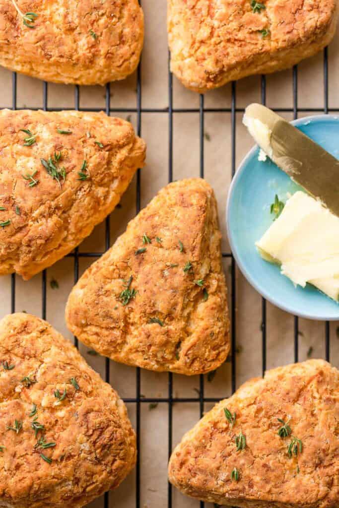 freshly baked gluten free cheese scones on a wire rack with small butter dish and fresh thyme scattered on top