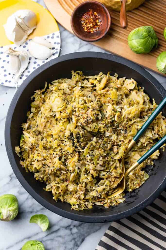 Sautéed Brussels Sprouts spiced with mustard, nigella and cumin seeds in a salad bowl with serving spoons