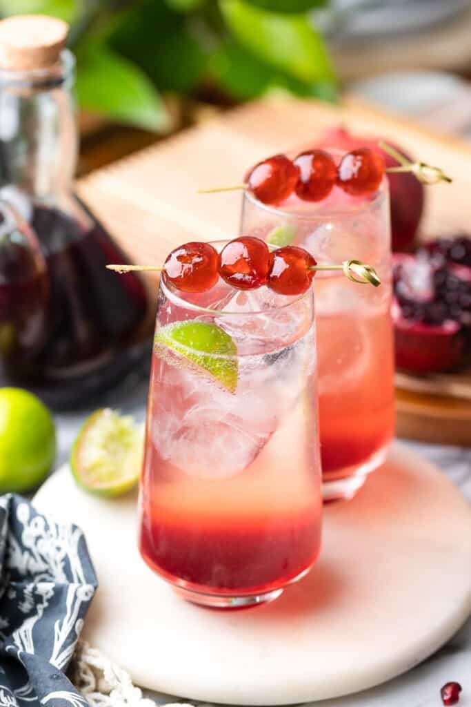two shirley temple cocktails in high ball glasses with cherries on toothpicks to garnish