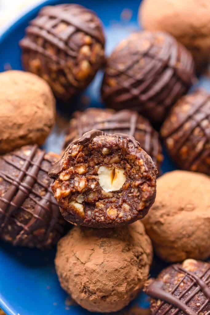 chocolate hazelnut date balls on a plate with one of the balls with a bite taken out to show off a roasted hazelnut hidden on the inside