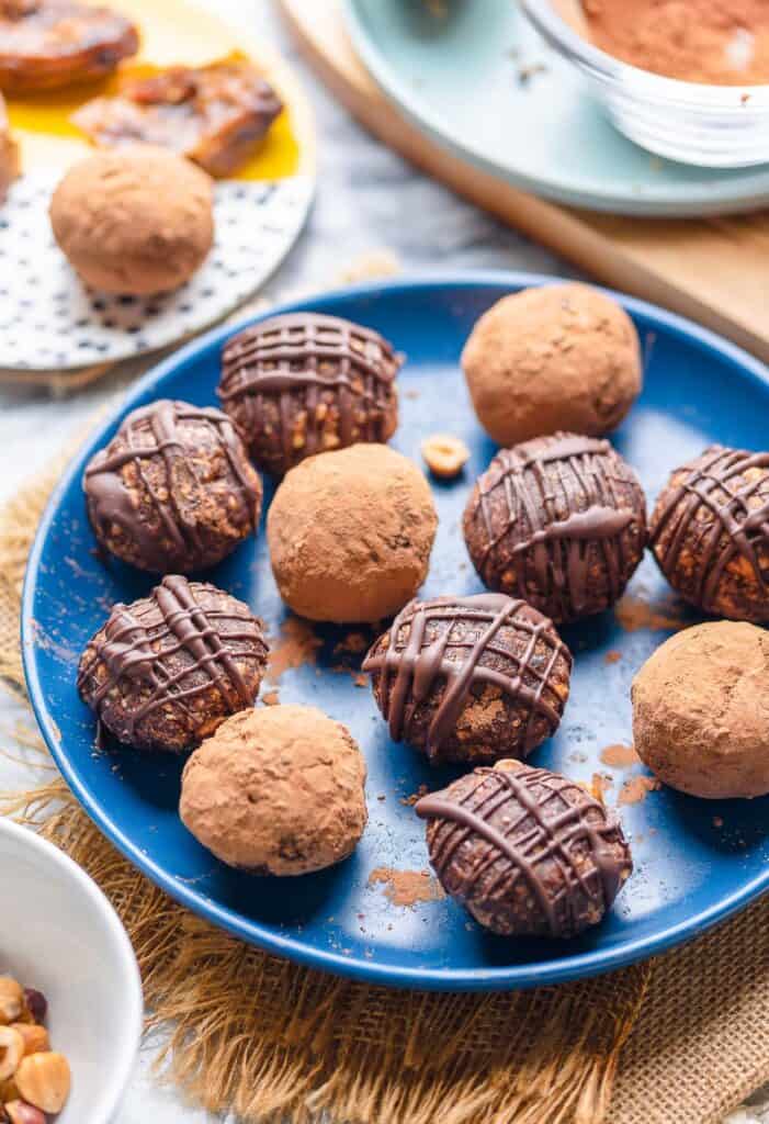 Chocolatey Hazelnut Date Balls on a plate some coated in cocoa powder and some drizzled with chocolate