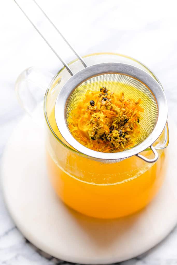 a small strainer over a tea pot staining out the solids in the ginger Turmeric Tea