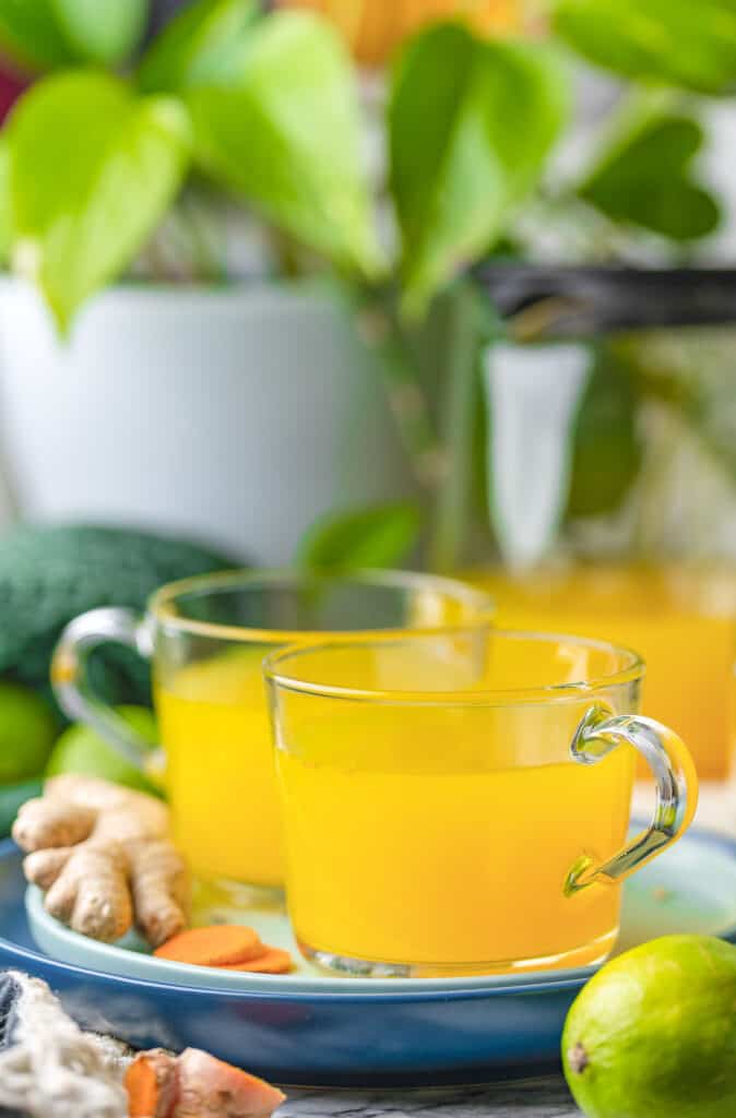 Ginger Turmeric Tea with Lime on a plate with fresh ginger and turmeric with a lime