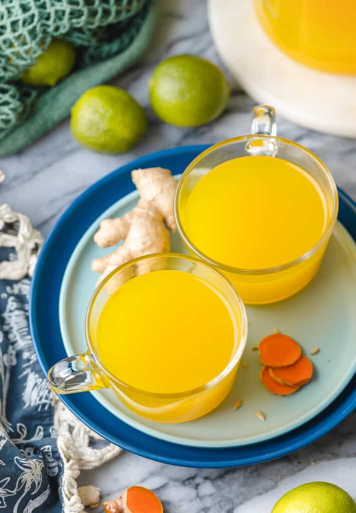 two small mugs of turmeric tea on a plate with free ginger and turmeric slices
