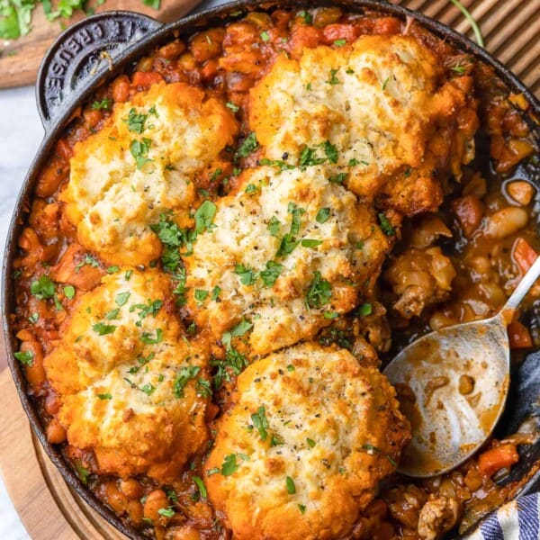 Italian Chicken & White Bean Stew with Parmesan Biscuits in a cast iron pan with a serving spoon