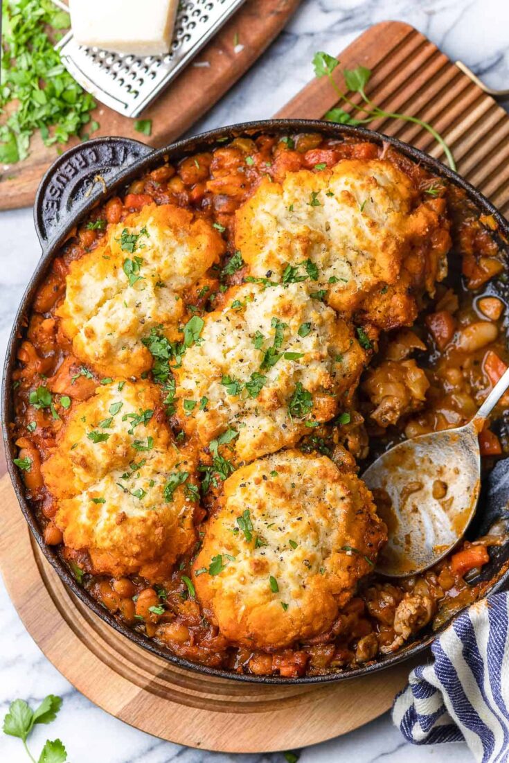 Italian Chicken & White Bean Stew with Parmesan Biscuits in a cast iron pan with a serving spoon
