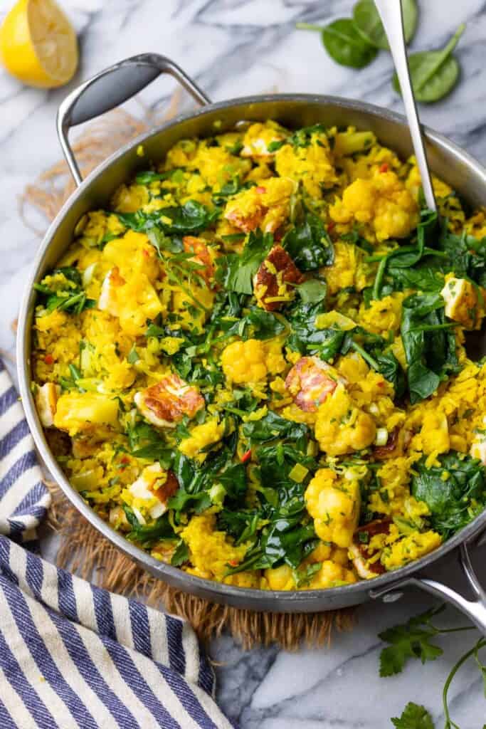 Curry Rice with Cauliflower and Halloumi in a stainless steel pan topped with fresh parsley and a squeezed lemon half on the side