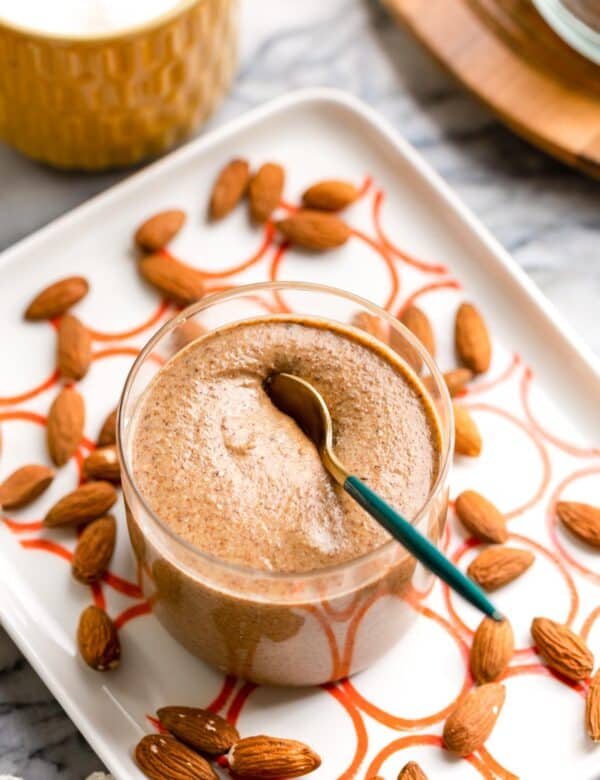 homemade almond butter in a small jar with a spoon on a serving plate with almonds