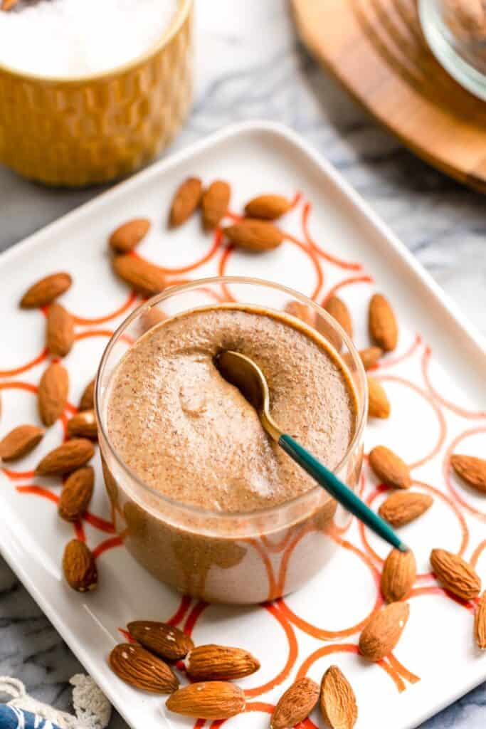 a serving plate with a jar of homemade almond butter and raw almonds on top