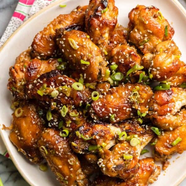 honey garlic chicken wings on a plate topped with green onions and sesame seeds